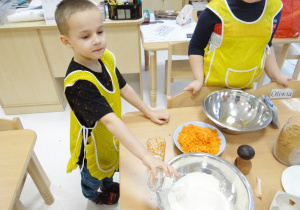 Zadowolony Igorek wsypuje mąkę do metalowej miski.